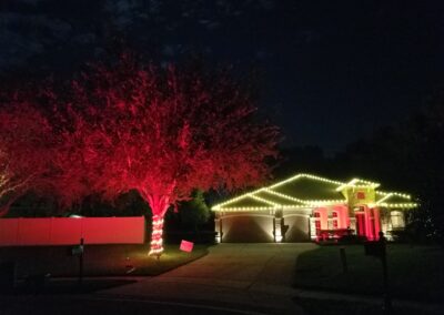 House with white christmas lights and a red tree